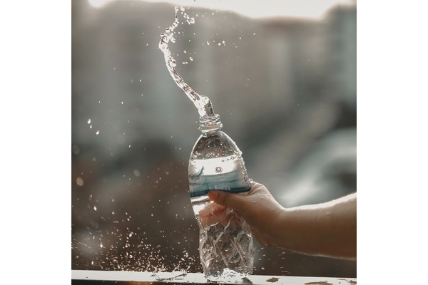 Image A hand squeezing a water bottle so water is sprouting out of the top.